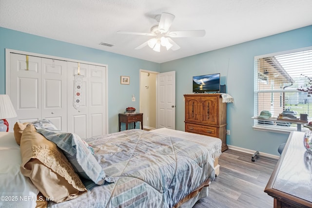 bedroom featuring wood finished floors, visible vents, baseboards, ceiling fan, and a closet