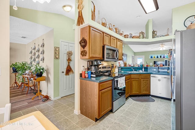 kitchen featuring vaulted ceiling, brown cabinets, stainless steel appliances, a ceiling fan, and a sink