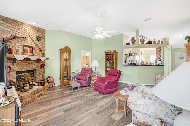 living area with visible vents, wood finished floors, a fireplace, ceiling fan, and vaulted ceiling