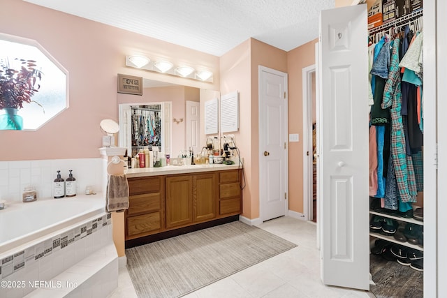 bathroom featuring tile patterned floors, a walk in closet, vanity, a bath, and a textured ceiling