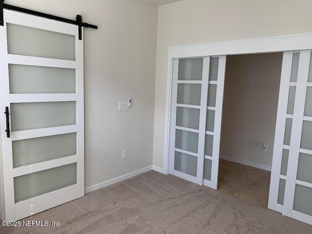 empty room featuring a barn door, carpet floors, and baseboards