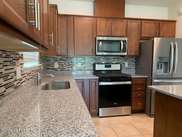 kitchen featuring a sink, stainless steel appliances, light stone counters, and decorative backsplash