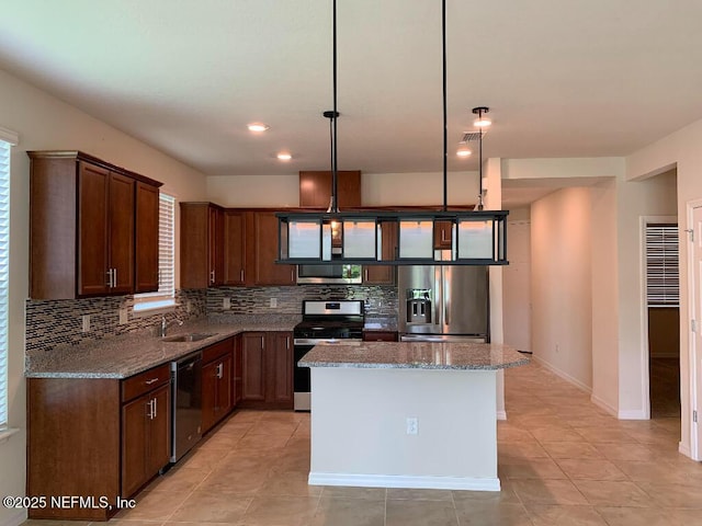 kitchen featuring a kitchen island, light stone countertops, decorative backsplash, appliances with stainless steel finishes, and a sink