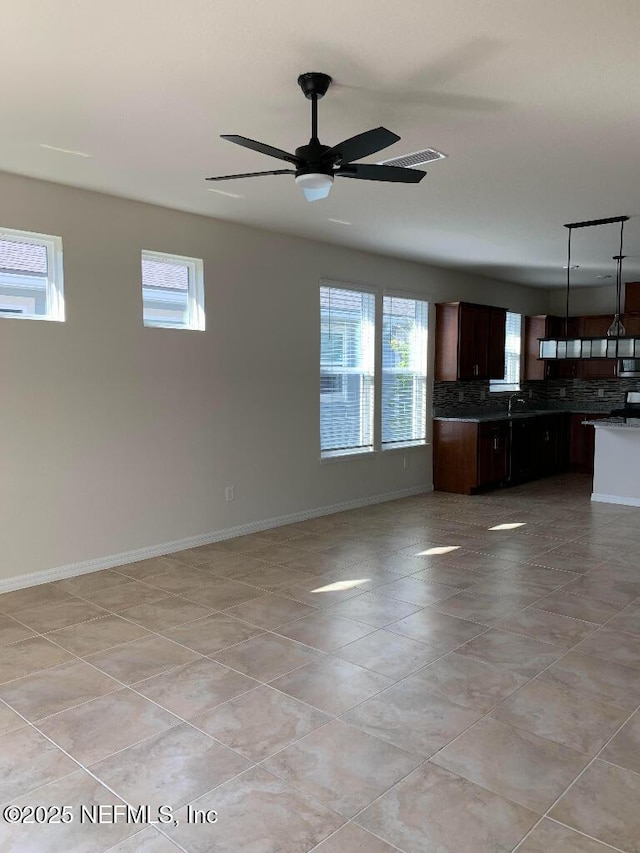 unfurnished living room with light tile patterned floors, a healthy amount of sunlight, baseboards, and ceiling fan