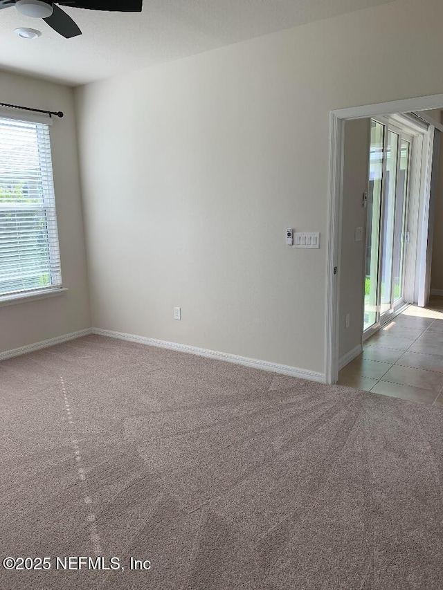 carpeted empty room featuring tile patterned flooring, baseboards, and ceiling fan