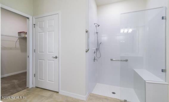 bathroom featuring a spacious closet, baseboards, and a stall shower