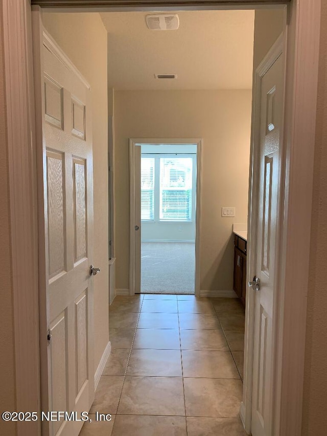 hall with light tile patterned flooring, baseboards, visible vents, and light carpet