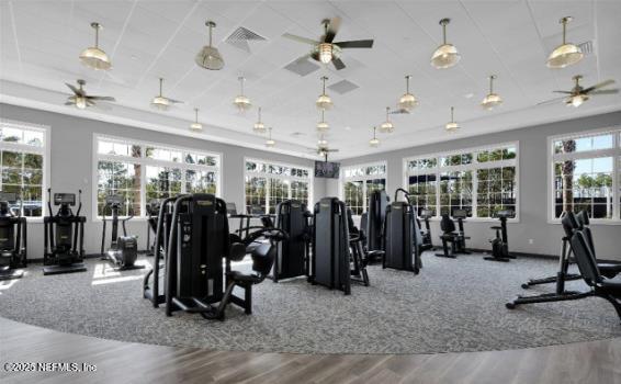 workout area featuring visible vents, a raised ceiling, wood finished floors, and a ceiling fan