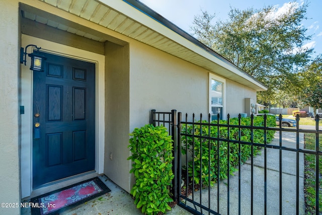 property entrance with stucco siding, fence, and a gate