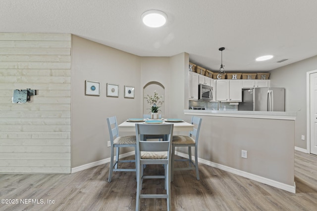 dining space with visible vents, light wood-style floors, baseboards, and a textured ceiling