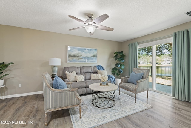 living room with wood finished floors, visible vents, baseboards, ceiling fan, and a textured ceiling