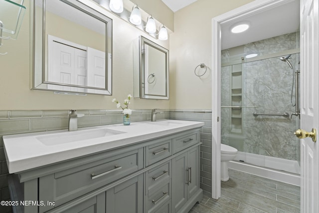 bathroom featuring a sink, tile walls, a shower stall, and double vanity