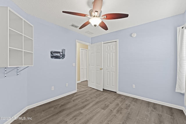 unfurnished bedroom featuring wood finished floors, visible vents, a closet, and baseboards