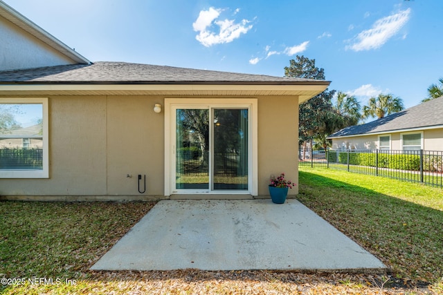 view of exterior entry with stucco siding, a lawn, a patio, and fence