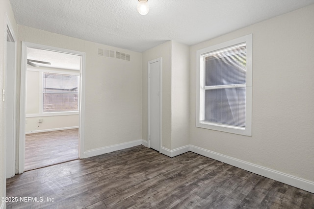 unfurnished room with a textured ceiling, wood finished floors, visible vents, and baseboards