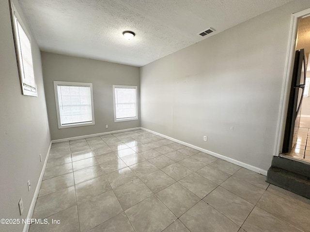 spare room with visible vents, a textured ceiling, and baseboards