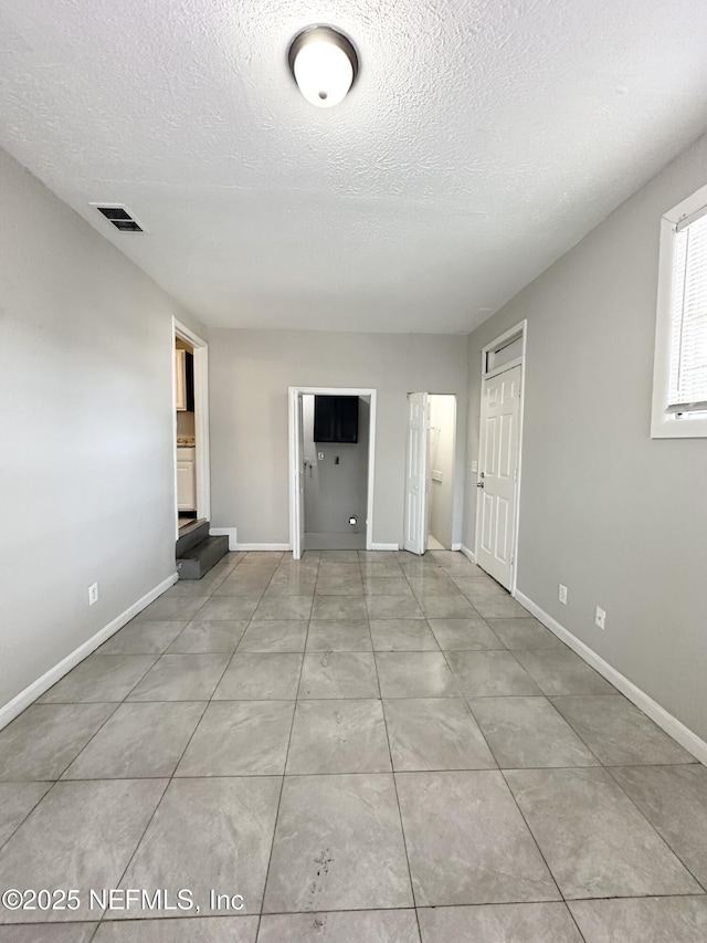 unfurnished living room featuring tile patterned flooring, baseboards, visible vents, and a textured ceiling