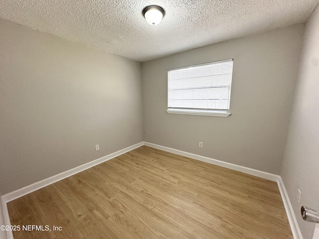 empty room with light wood-style flooring, a textured ceiling, and baseboards