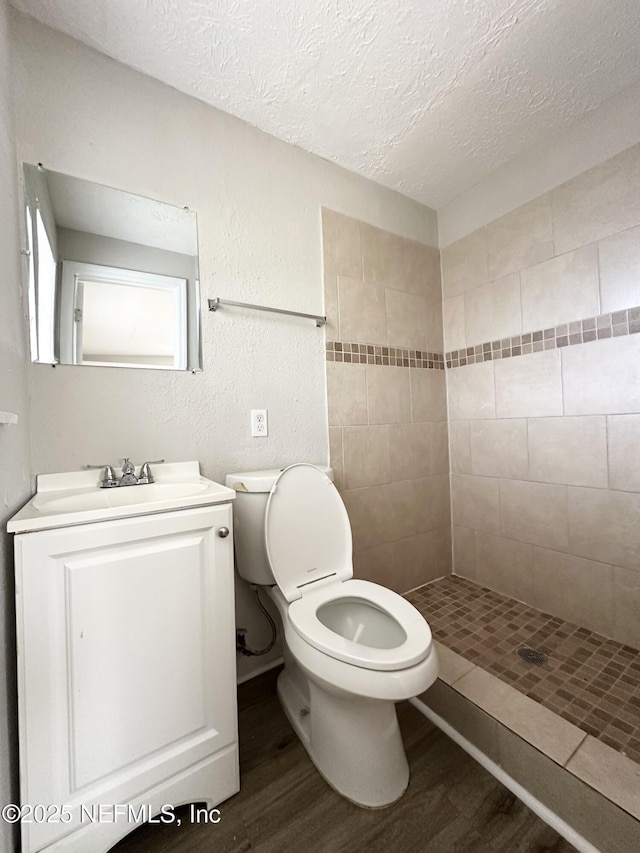 full bathroom with toilet, vanity, tiled shower, wood finished floors, and a textured ceiling