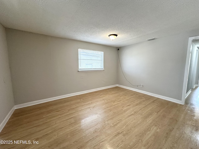 unfurnished room featuring visible vents, baseboards, a textured ceiling, and wood finished floors