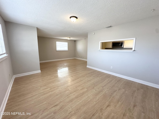 unfurnished room featuring visible vents, a textured ceiling, light wood-type flooring, and baseboards