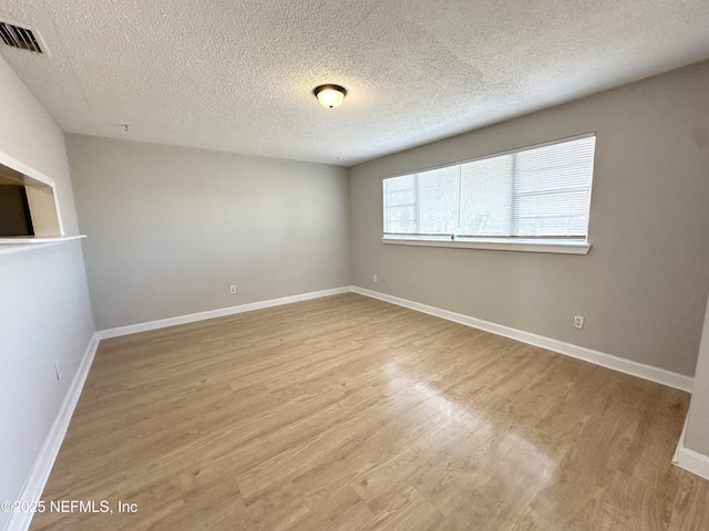 unfurnished room with baseboards, visible vents, light wood finished floors, and a textured ceiling