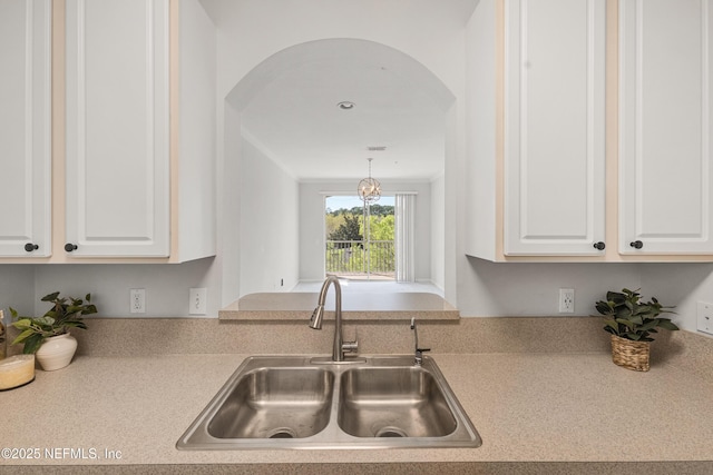 kitchen featuring white cabinetry, light countertops, arched walkways, and a sink