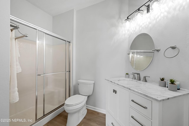 bathroom with toilet, a stall shower, wood finished floors, baseboards, and vanity