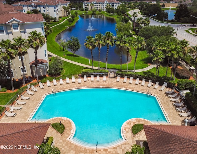 community pool with a patio, fence, and a water view