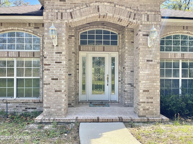 entrance to property with brick siding and a shingled roof