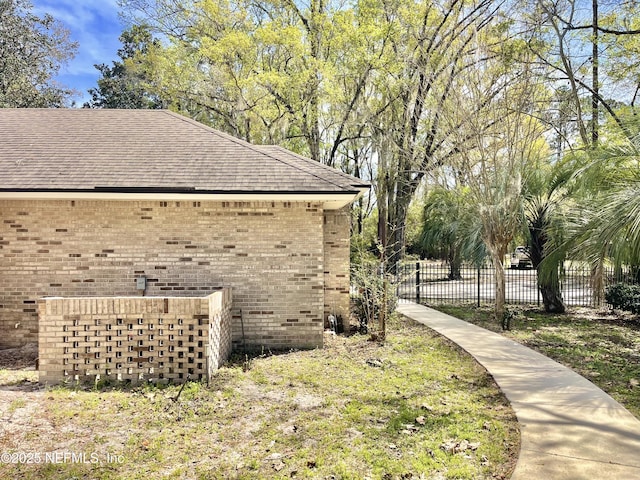 view of side of home with brick siding, a shingled roof, and fence