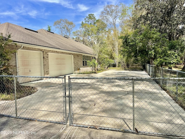 view of side of home featuring driveway, a gate, fence, an attached garage, and brick siding