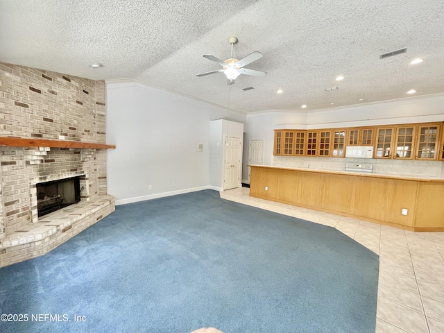 unfurnished living room featuring light tile patterned flooring, a fireplace, ceiling fan, crown molding, and light colored carpet