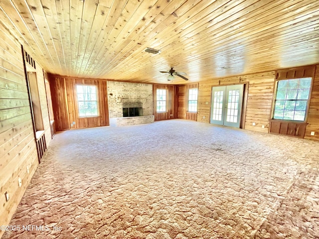 unfurnished living room with a healthy amount of sunlight, wood walls, and a ceiling fan