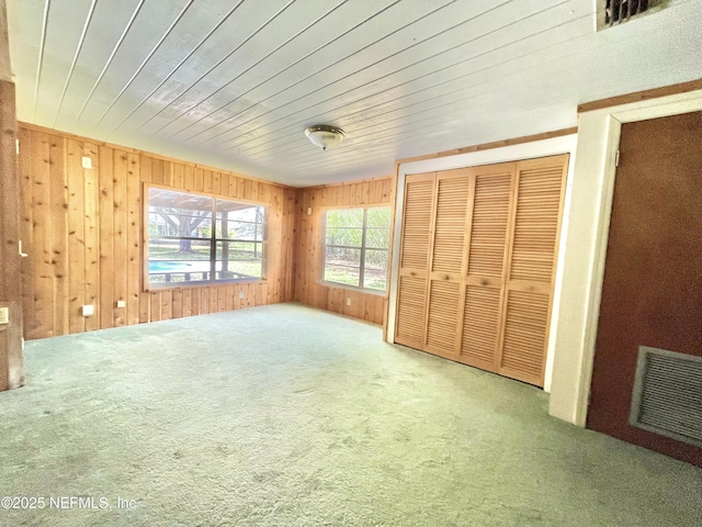 unfurnished bedroom featuring a closet, visible vents, wood walls, and carpet