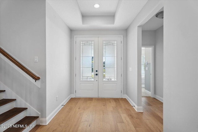 foyer entrance with a tray ceiling, french doors, stairway, light wood finished floors, and baseboards