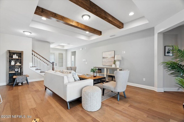 living area featuring stairs, beam ceiling, baseboards, and light wood finished floors