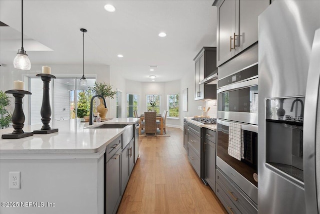 kitchen with light wood finished floors, decorative light fixtures, recessed lighting, appliances with stainless steel finishes, and a sink