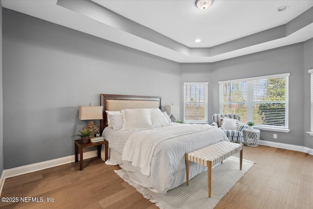 bedroom featuring recessed lighting, a tray ceiling, baseboards, and wood finished floors