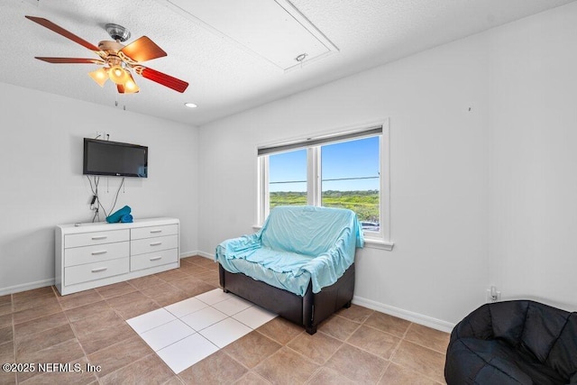 sitting room featuring attic access, a textured ceiling, baseboards, ceiling fan, and light tile patterned floors