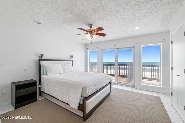 bedroom featuring a textured ceiling, access to exterior, a ceiling fan, and a water view