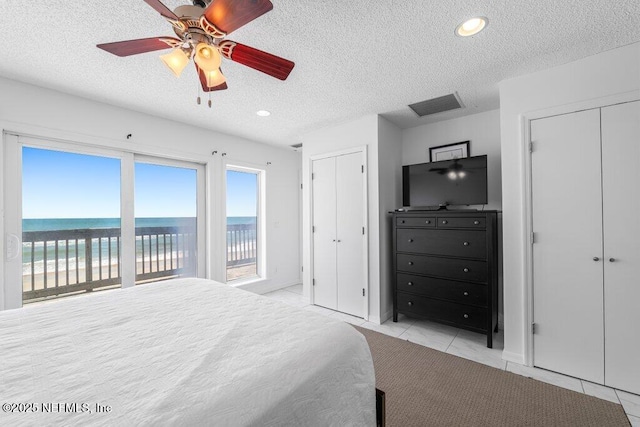 bedroom featuring a textured ceiling, light tile patterned flooring, visible vents, access to outside, and two closets