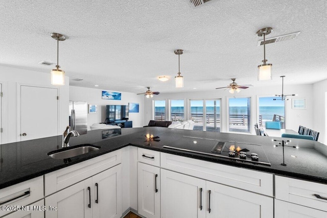 kitchen featuring visible vents, a sink, black electric stovetop, stainless steel fridge, and a textured ceiling