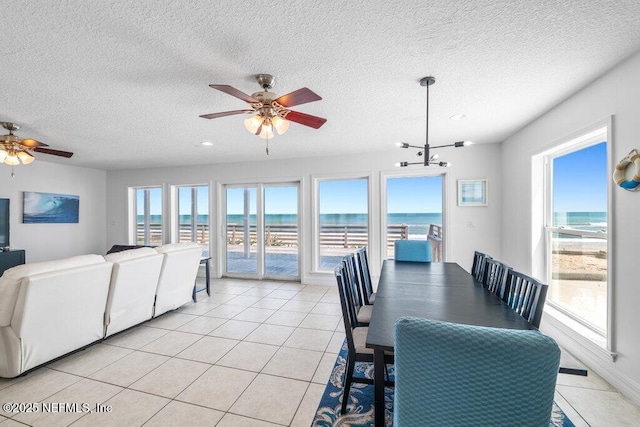 dining area featuring a water view, light tile patterned floors, and ceiling fan with notable chandelier