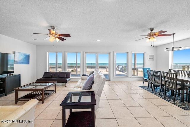 living area with ceiling fan, light tile patterned flooring, a textured ceiling, and a water view