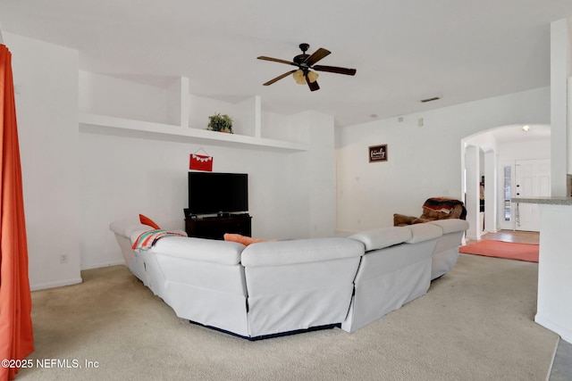 carpeted living room with visible vents, a ceiling fan, and arched walkways