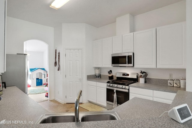 kitchen featuring light countertops, appliances with stainless steel finishes, arched walkways, white cabinets, and a sink