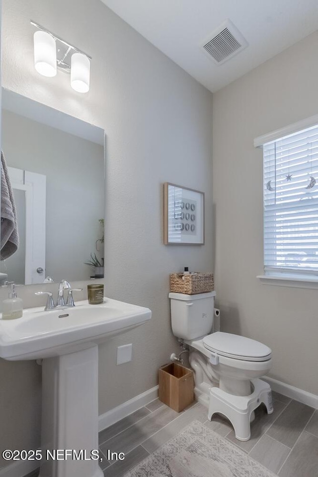 half bathroom featuring toilet, baseboards, visible vents, and a sink