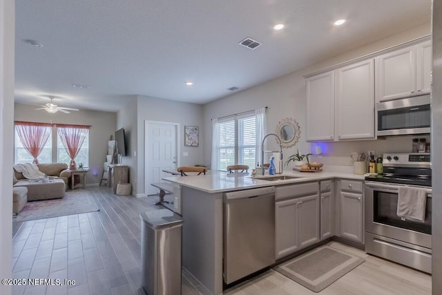 kitchen with visible vents, a peninsula, stainless steel appliances, light countertops, and open floor plan