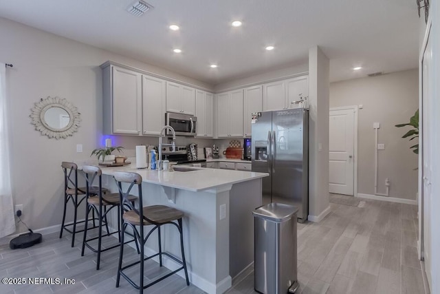 kitchen with light wood-style flooring, appliances with stainless steel finishes, a breakfast bar area, a peninsula, and light countertops